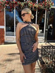Woman wearing black and white polka dot satin mini dress with halter scarf neckline. 