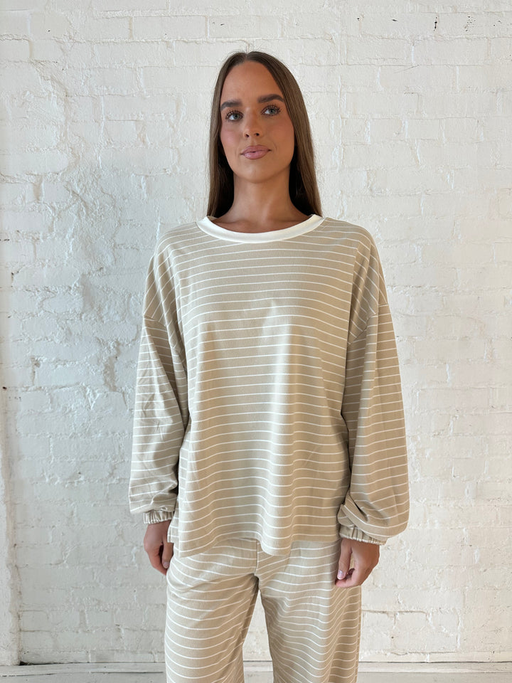 Woman wearing two piece tan striped long sleeve lounge set.