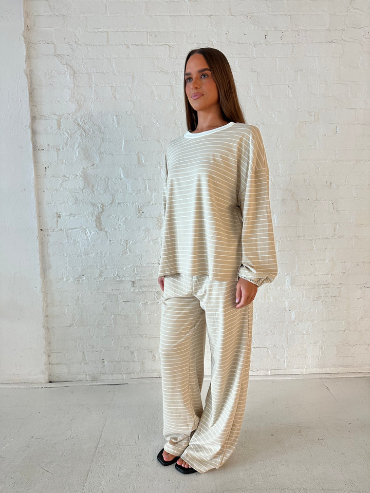 Woman wearing two piece tan striped long sleeve lounge set.