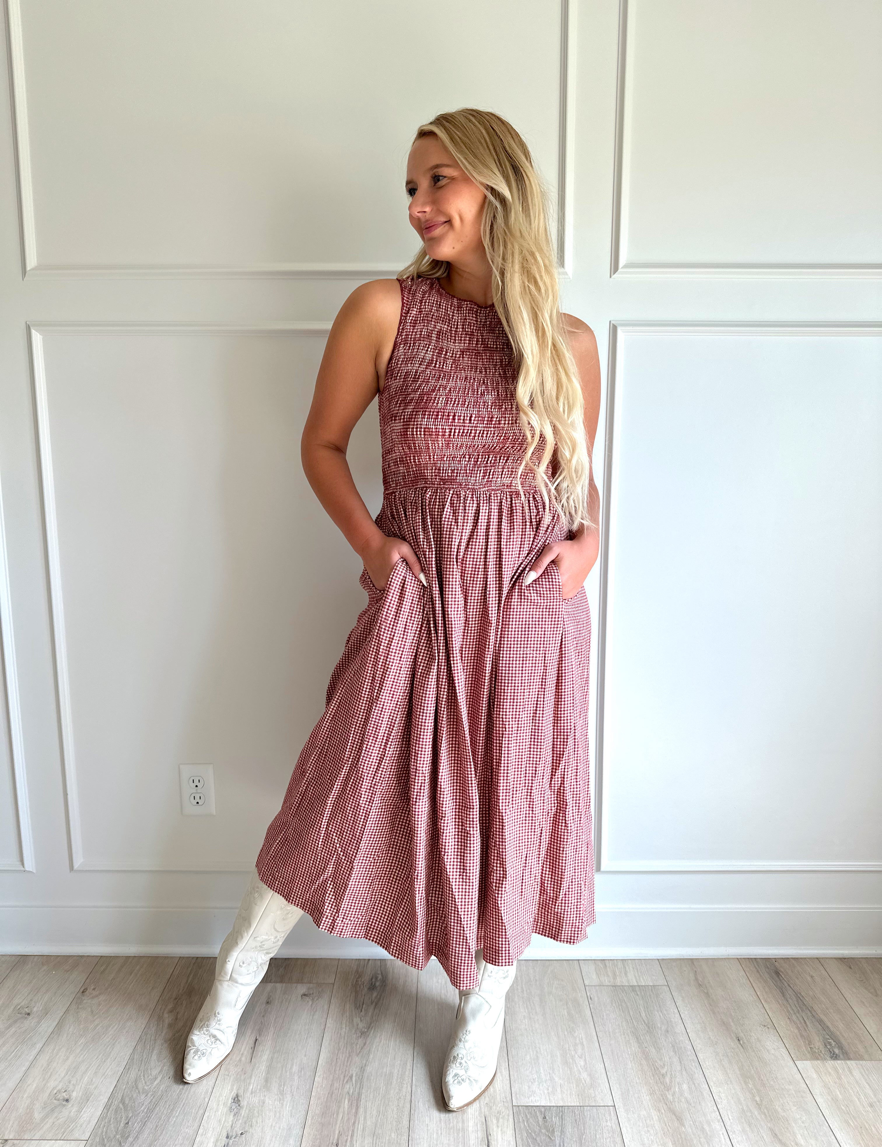 Woman wearing burgundy gingham midi dress with open back and tie neck closure, with functional pockets.