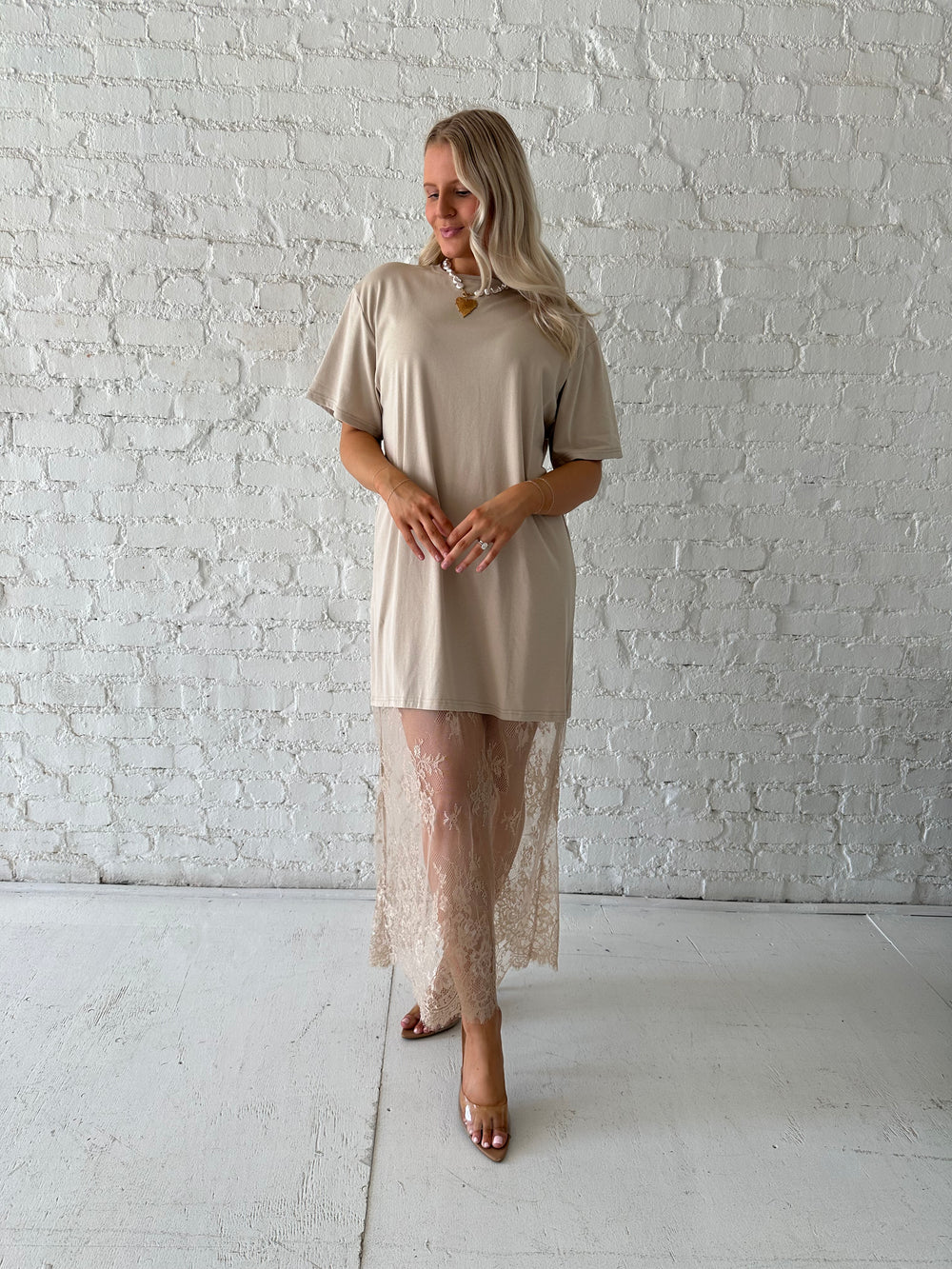 Woman wearing beige t-shirt dress with lace underlay, and oversized fit. 