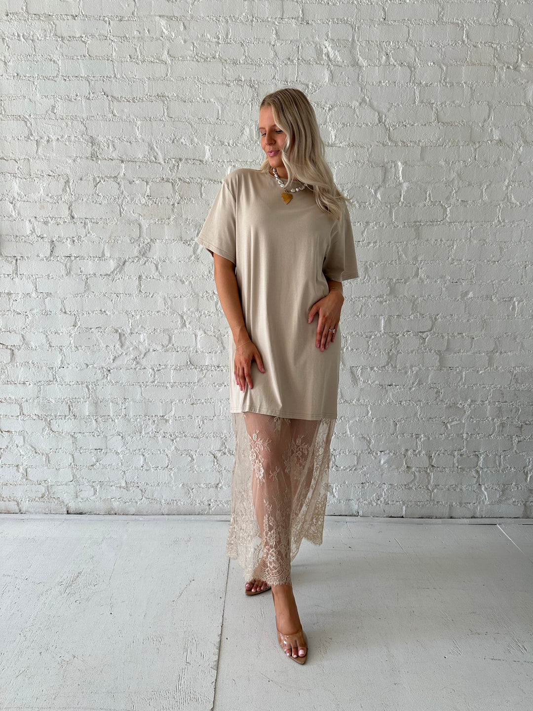 Woman wearing beige t-shirt dress with lace underlay, and oversized fit. 
