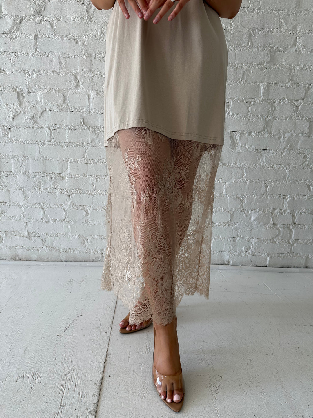 Woman wearing beige t-shirt dress with lace underlay, and oversized fit. 