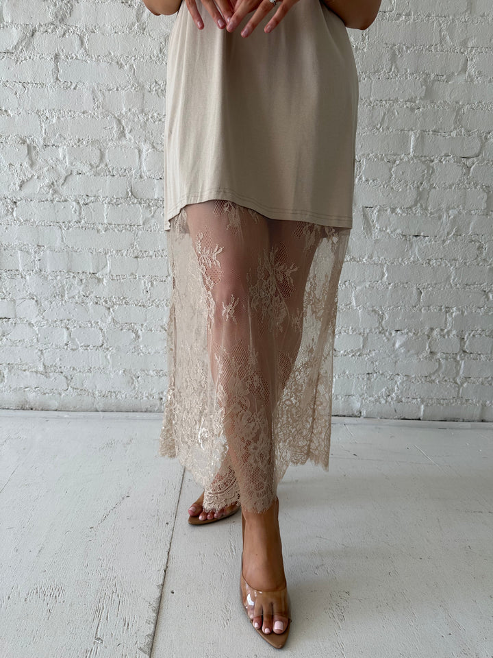 Woman wearing beige t-shirt dress with lace underlay, and oversized fit. 