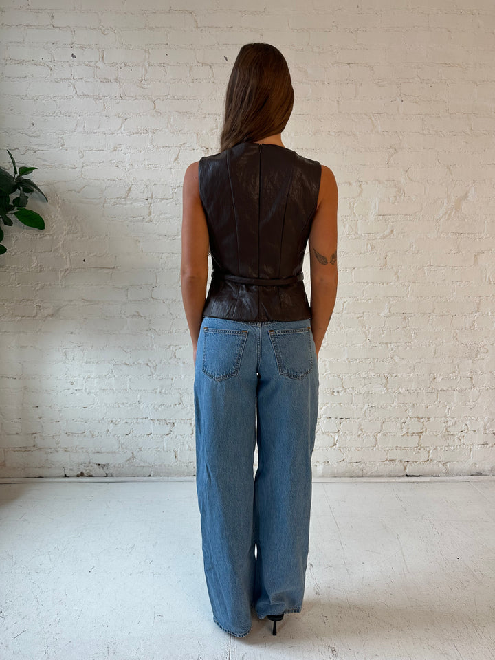 Woman wearing dark brown faux leather top with belted waist, and medium wash jeans.