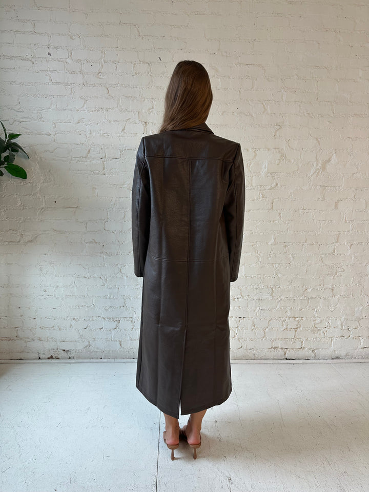 Woman wearing dark brown faux leather trench coat over brown abstract satin mini dress. 
