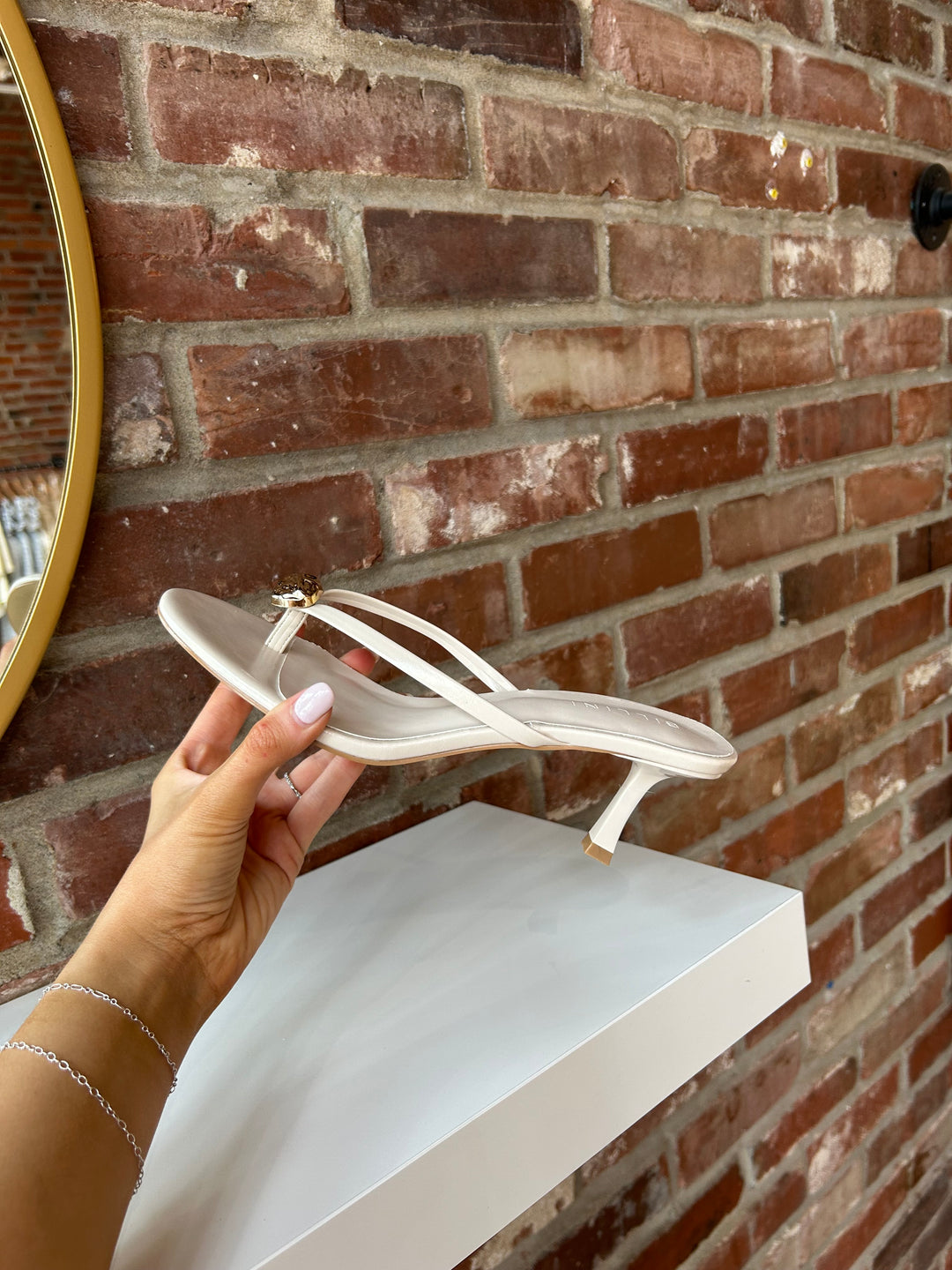 Cream colored flip flop kitten heel with a gold accent hardware detail. 