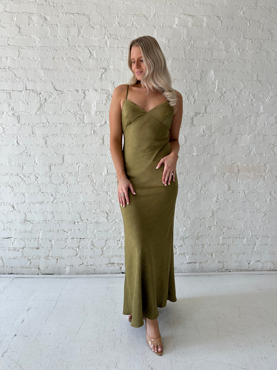 Woman wearing olive green maxi dress with v-neckline and adjustable straps. 