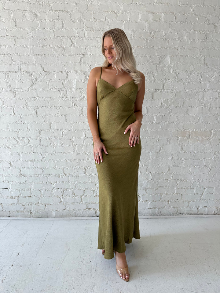 Woman wearing olive green maxi dress with v-neckline and adjustable straps. 