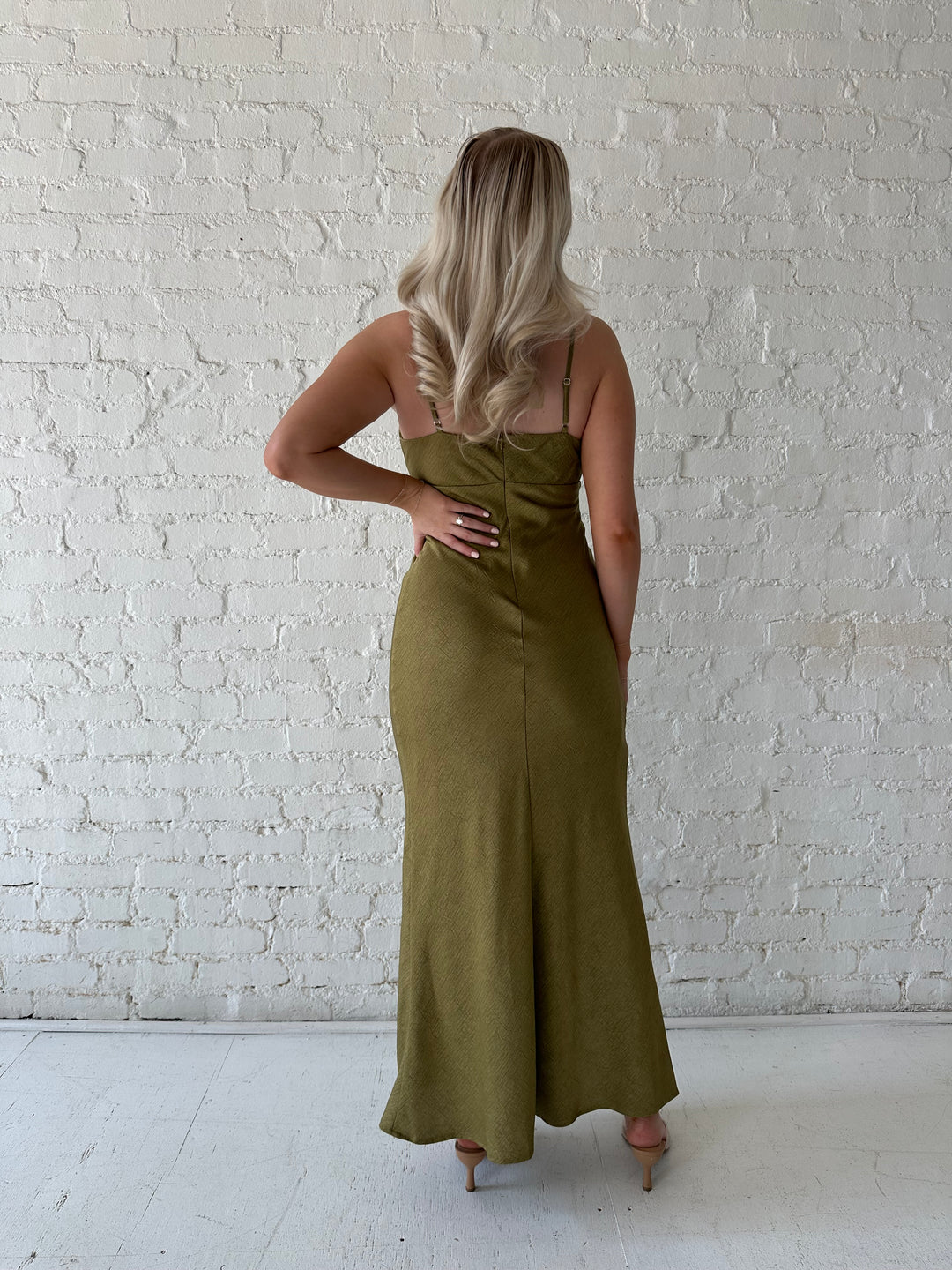 Woman wearing olive green maxi dress with v-neckline and adjustable straps. 