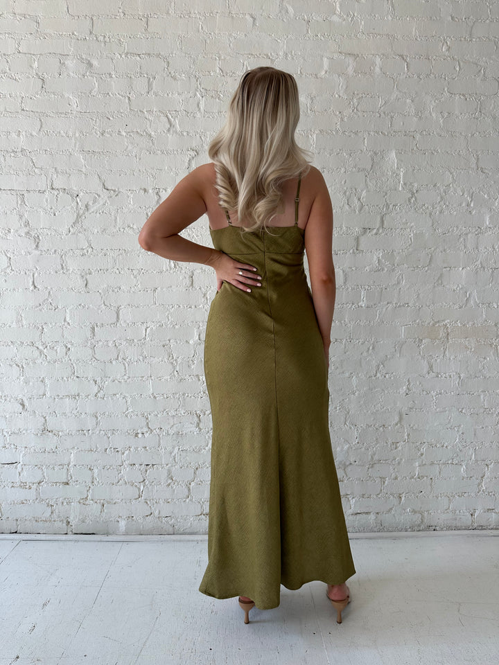 Woman wearing olive green maxi dress with v-neckline and adjustable straps. 