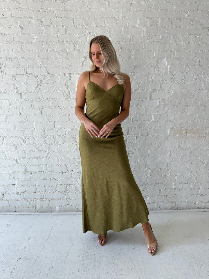 Woman wearing olive green maxi dress with v-neckline and adjustable straps. 