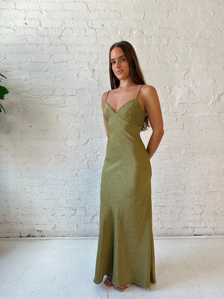 Woman wearing olive green textured maxi dress with v-neckline and adjustable spaghetti straps. 