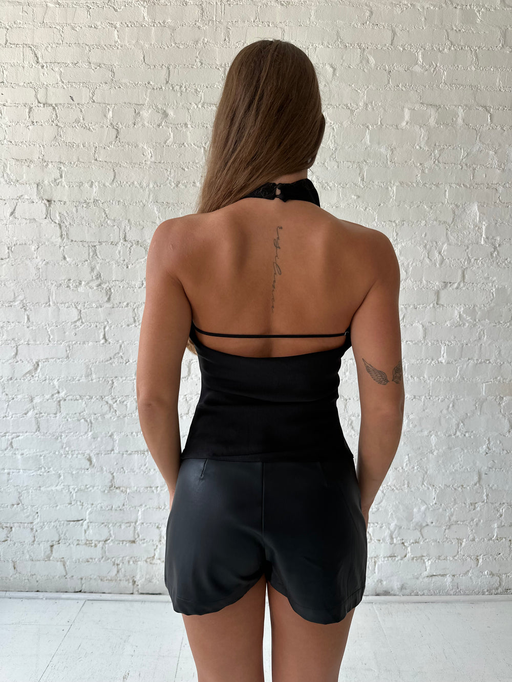 Woman wearing black satin cowl halter neck top with open back and strap detail. 
