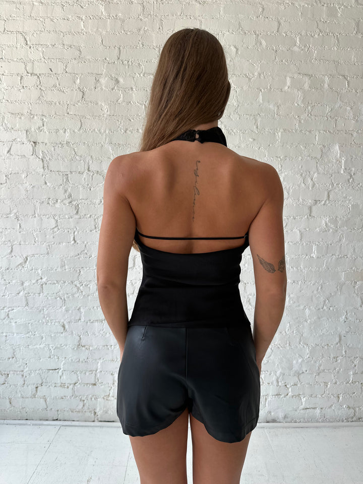 Woman wearing black satin cowl halter neck top with open back and strap detail. 