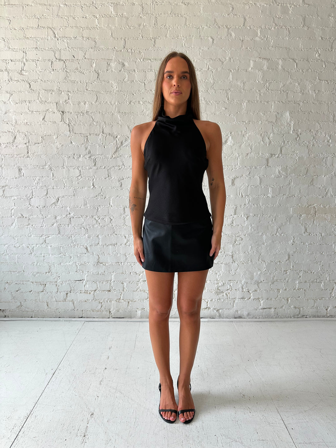 Woman wearing black satin cowl halter neck top with open back and strap detail. 