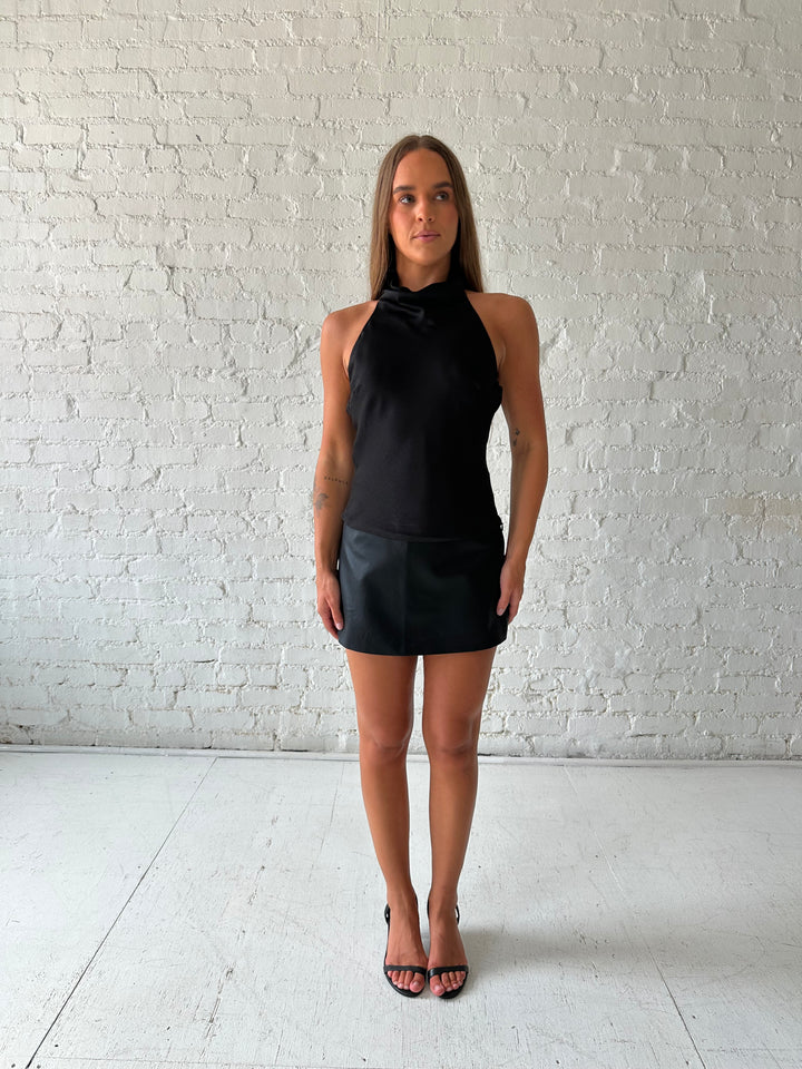Woman wearing black satin cowl halter neck top with open back and strap detail. 