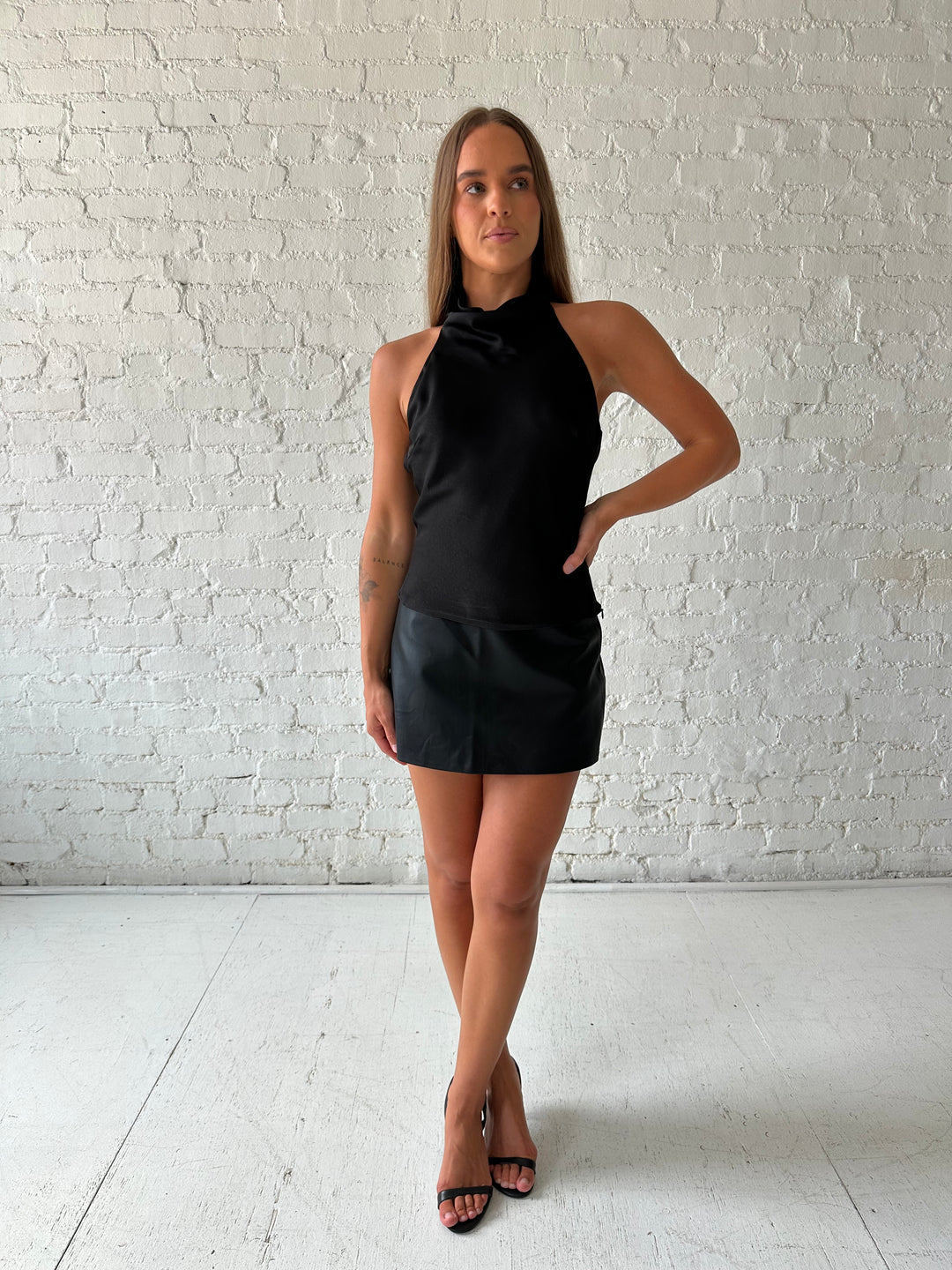 Woman wearing black satin cowl halter neck top with open back and strap detail. 