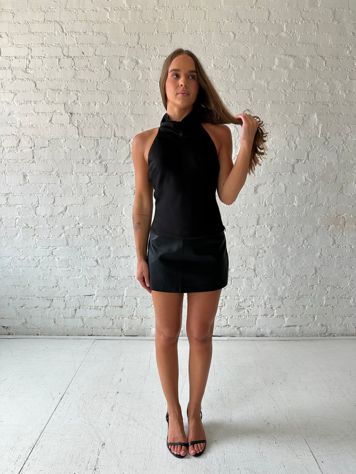 Woman wearing black satin cowl halter neck top with open back and strap detail. 