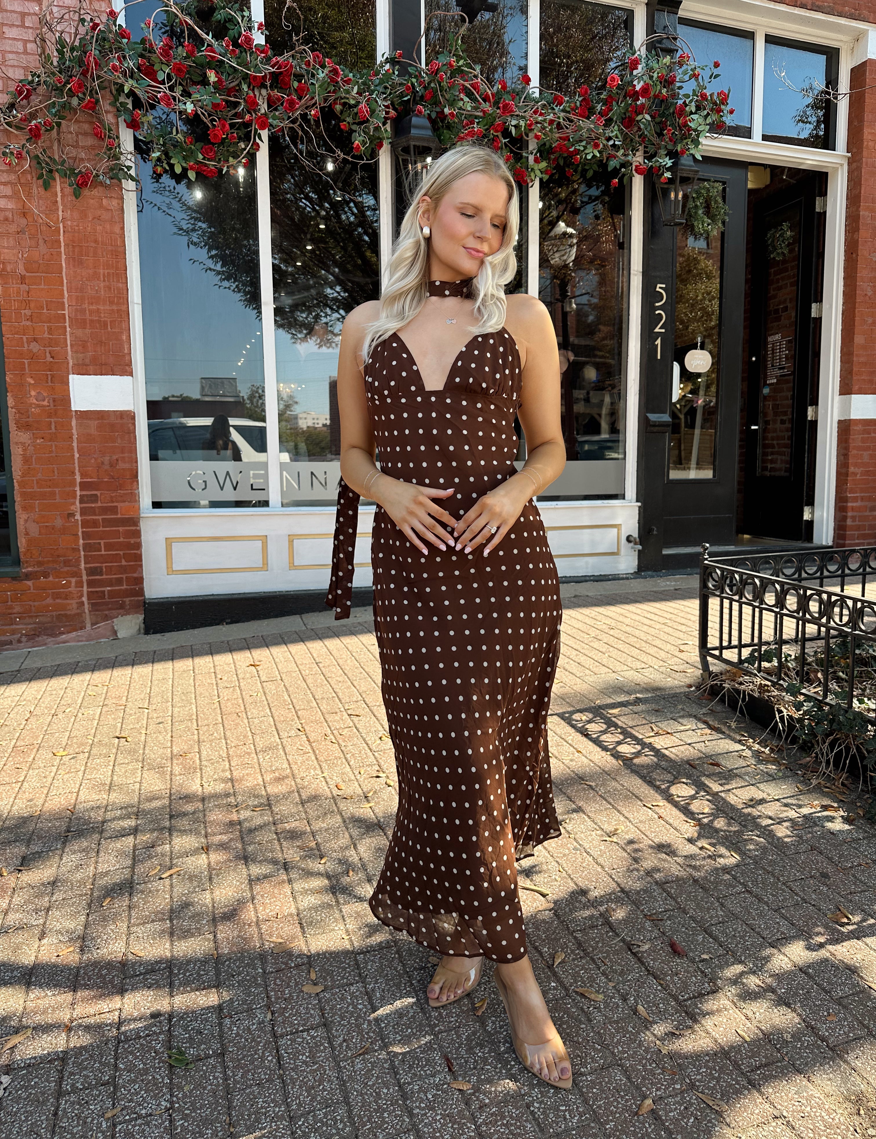 Woman wearing brown polka dot maxi dress with detachable neck scarf.