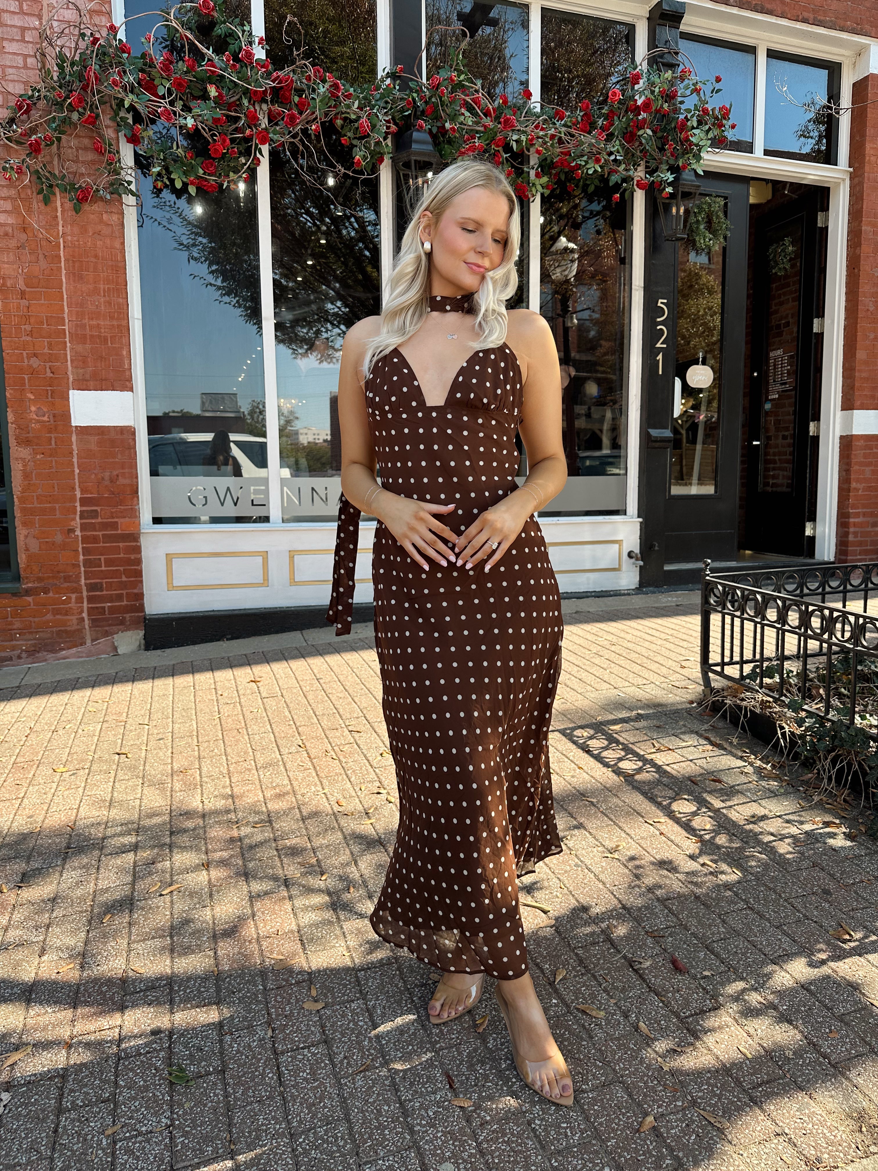 Woman wearing brown polka dot maxi dress with detachable neck scarf.