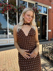 Woman wearing brown polka dot maxi dress with detachable neck scarf.