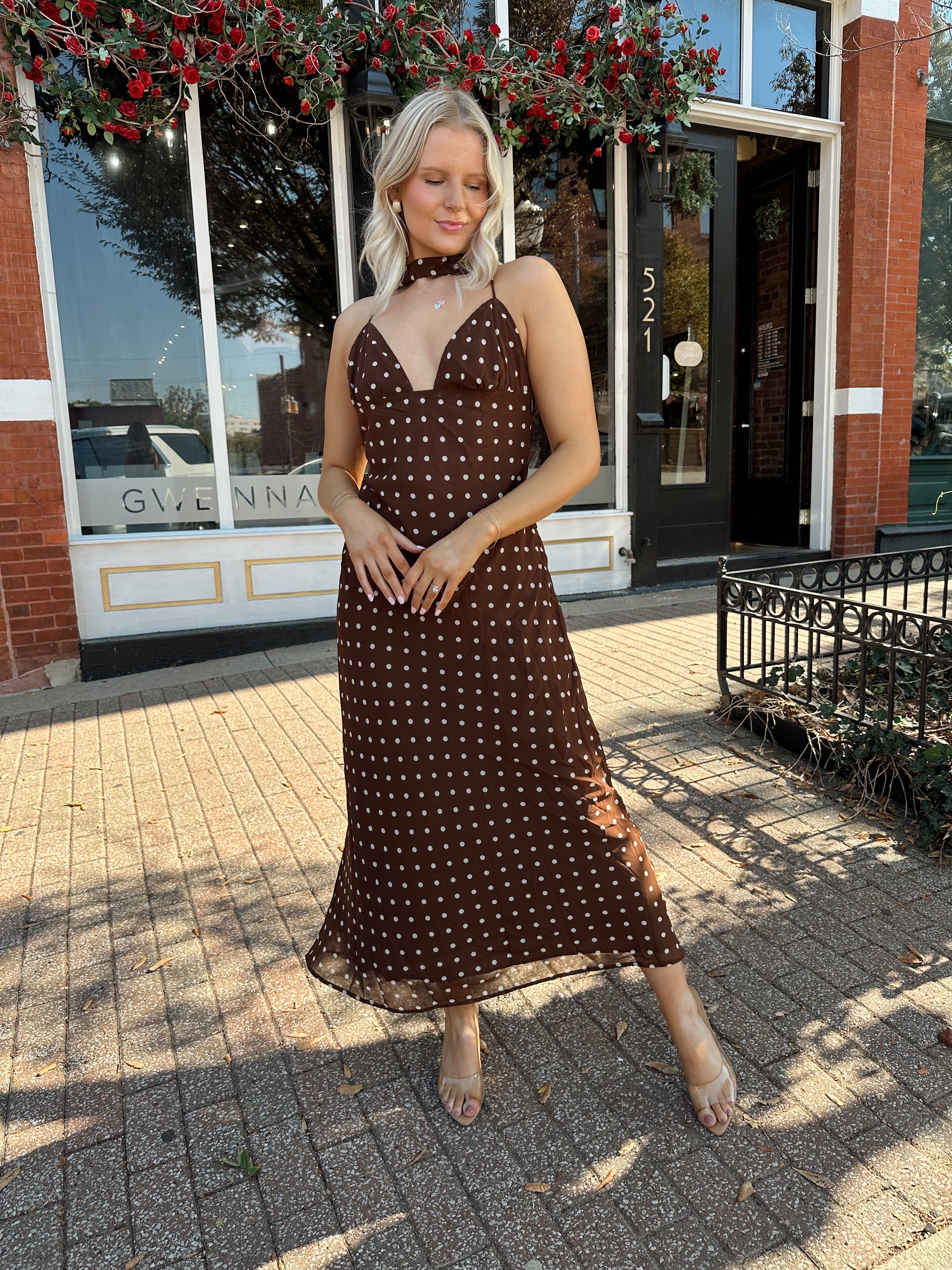 Woman wearing brown polka dot maxi dress with detachable neck scarf.