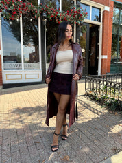 Woman wearing burgundy leather trench coat with belt and and button closure. 