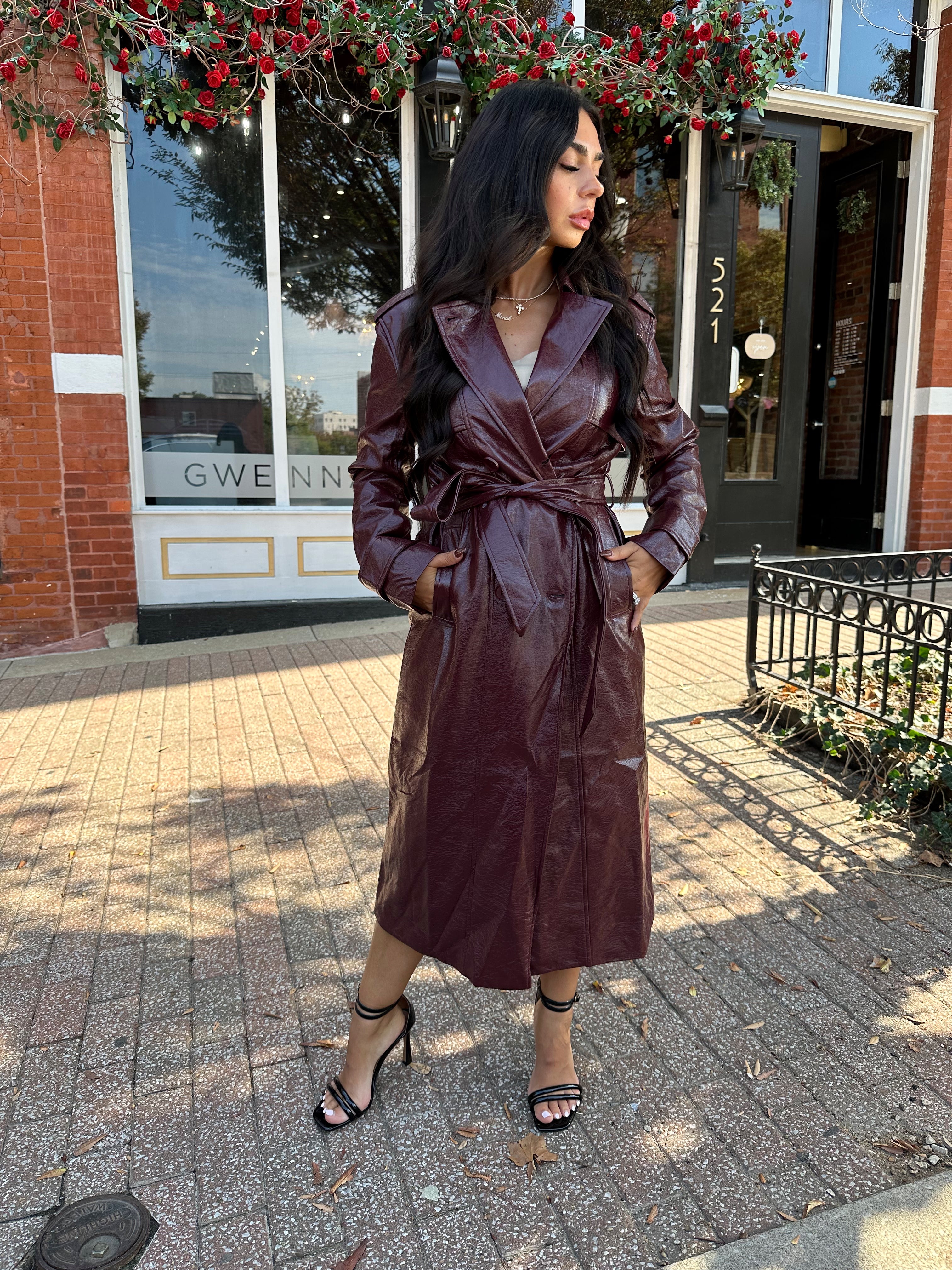 Woman wearing burgundy leather trench coat with belt and and button closure. 