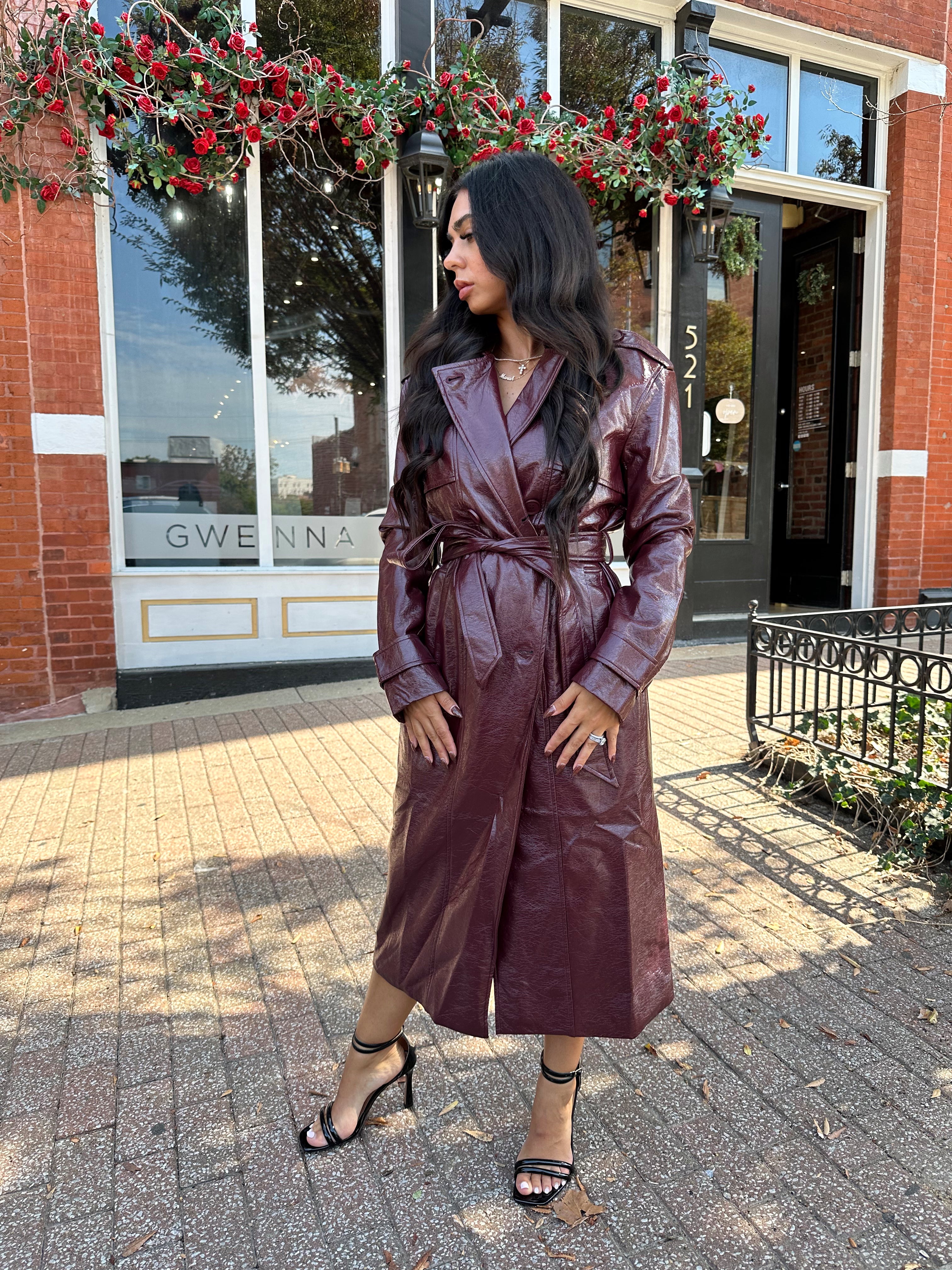 Woman wearing burgundy leather trench coat with belt and and button closure. 