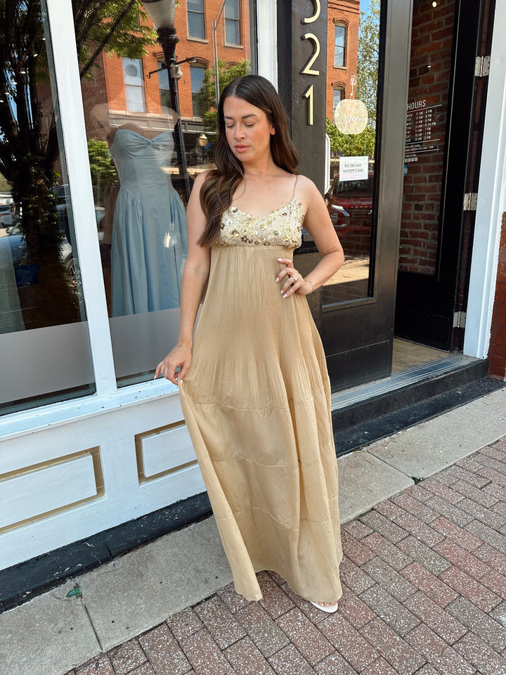 Woman wearing gold pleated maxi dress with sequin bust and adjustable spaghetti straps. 