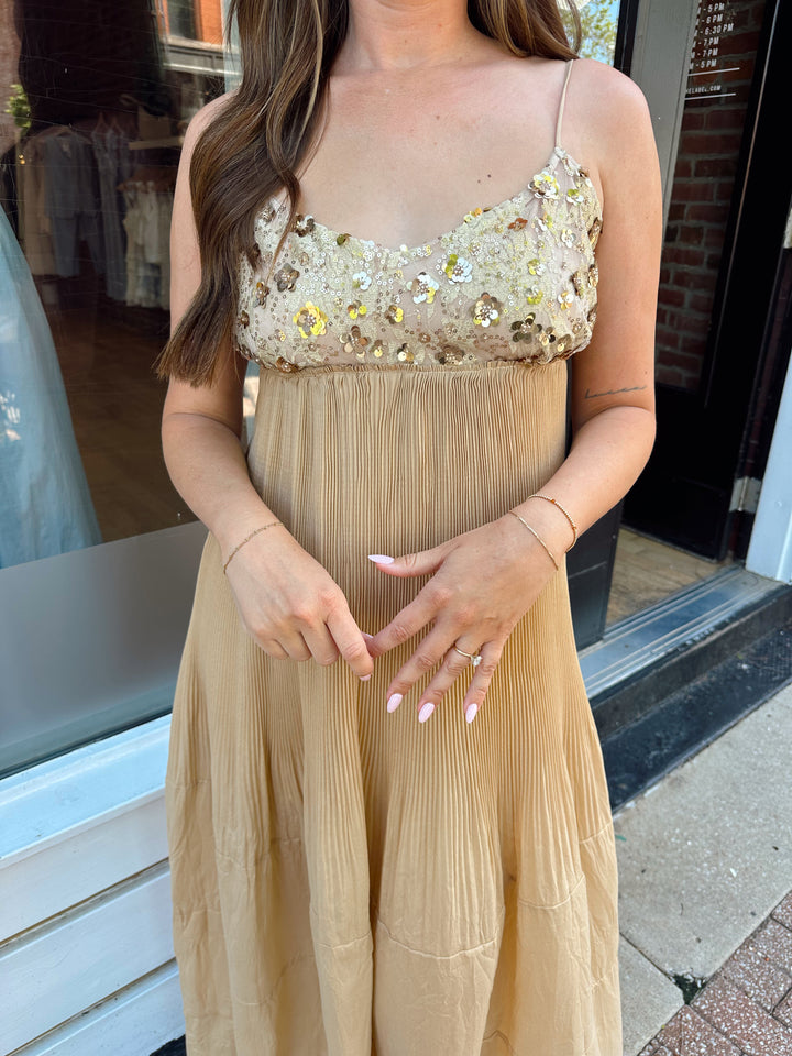 Woman wearing gold pleated maxi dress with sequin bust and adjustable spaghetti straps. 