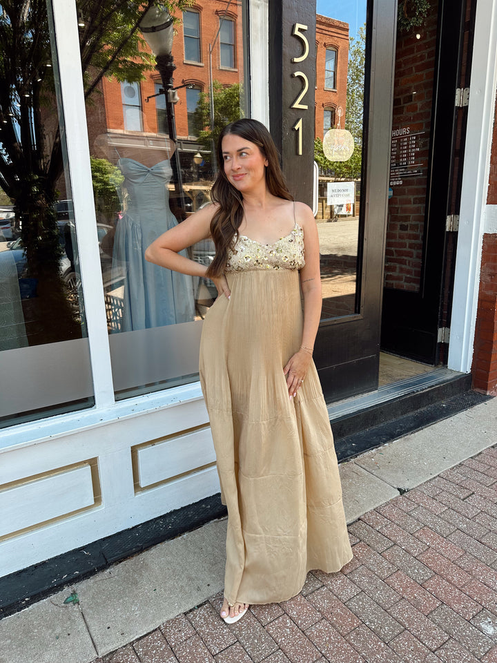 Woman wearing gold pleated maxi dress with sequin bust and adjustable spaghetti straps. 