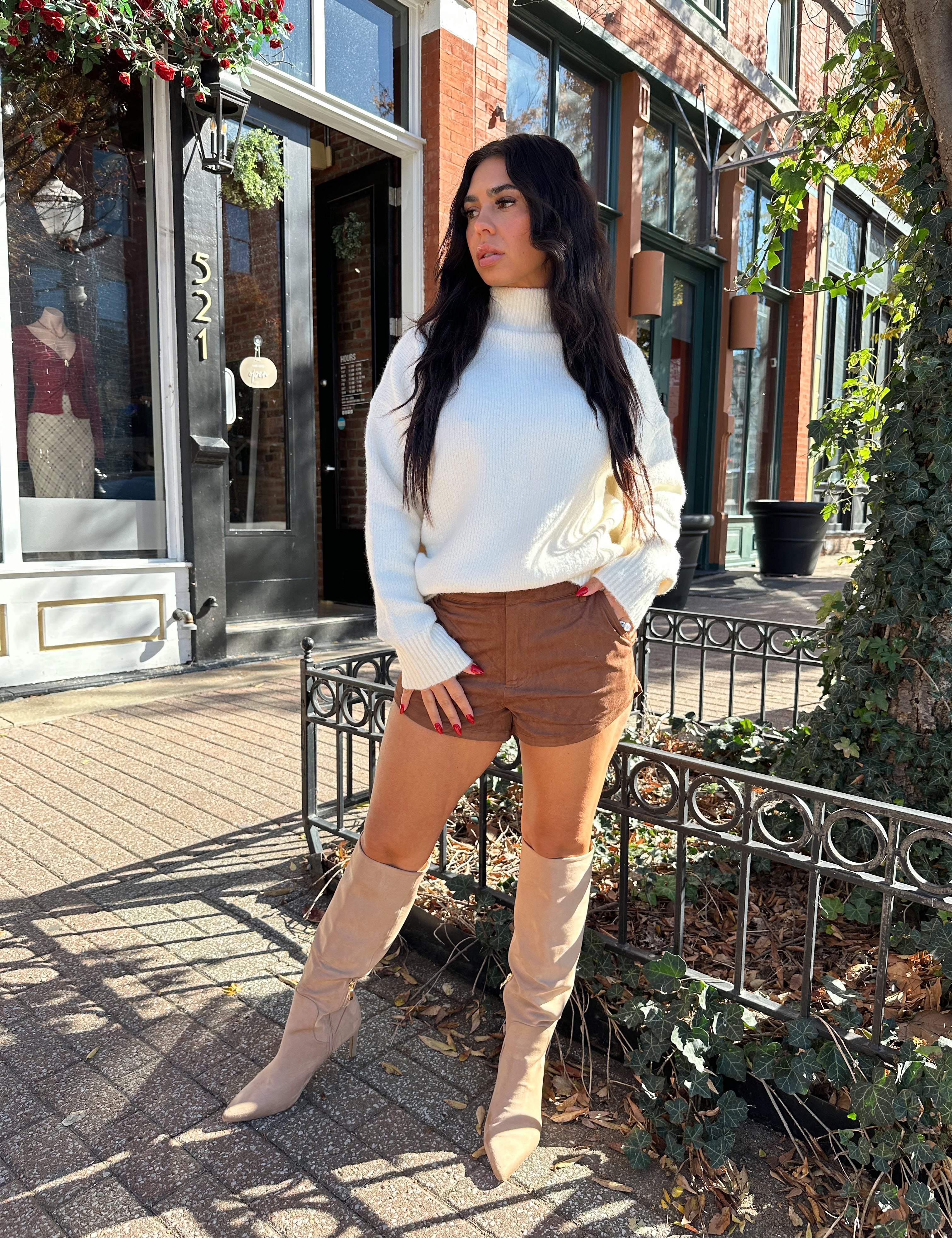 Woman wearing cream colored turtle neck sweater and brown suede micro short. 