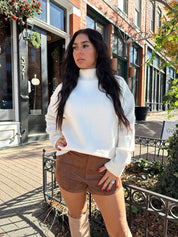Woman wearing cream colored turtle neck sweater and brown suede micro short. 