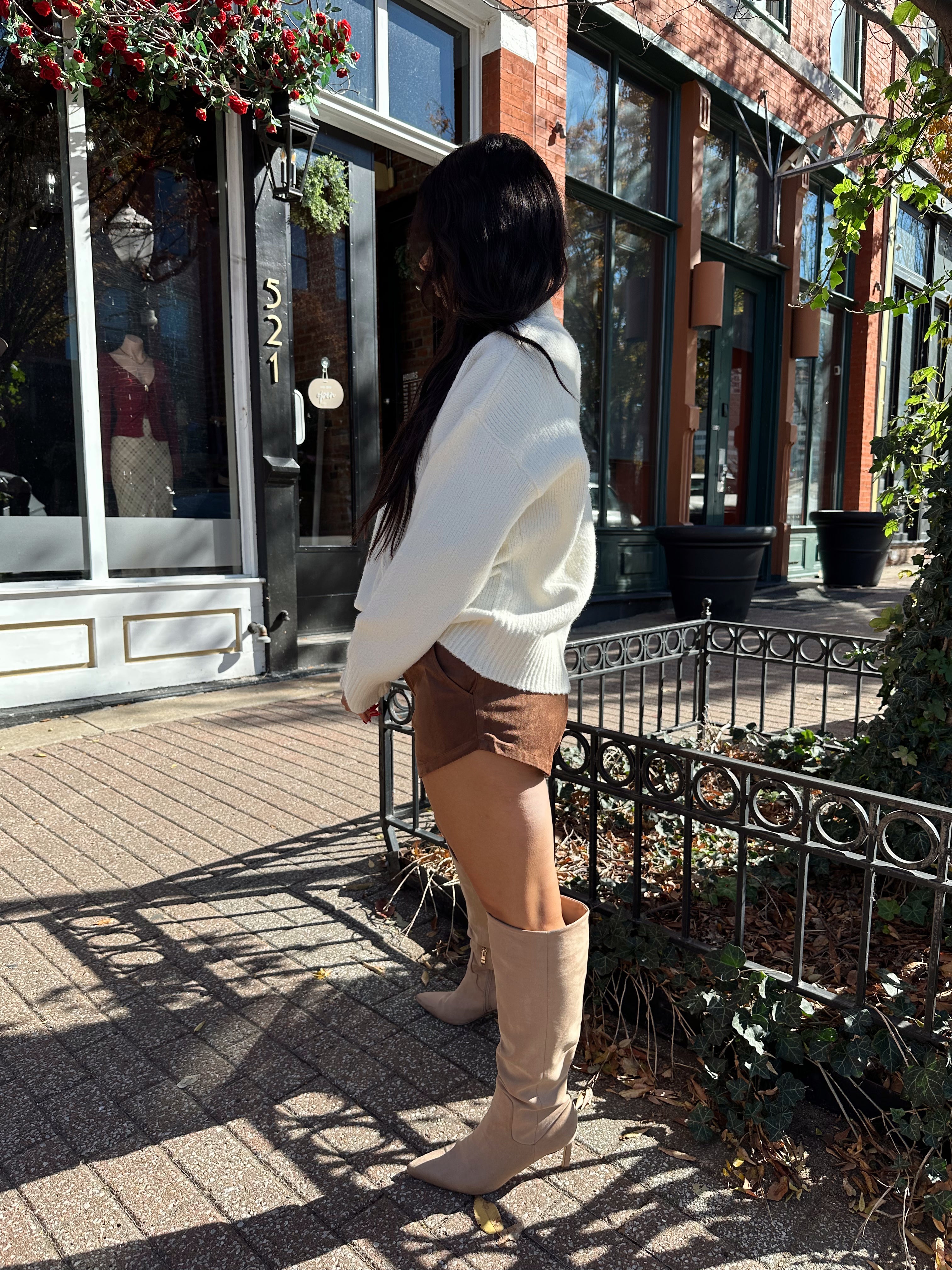 Woman wearing cream colored turtle neck sweater and brown suede micro short. 