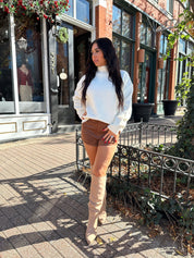 Woman wearing cream colored turtle neck sweater and brown suede micro short. 