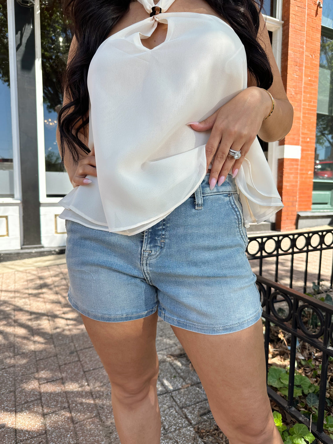 Woman wearing medium wash denim short with chiffon alter top.