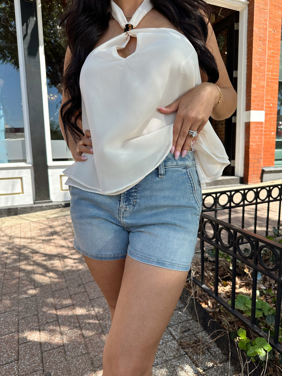 Woman wearing medium wash denim short with chiffon alter top.