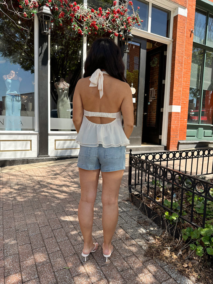 Woman wearing medium wash denim short with chiffon alter top.