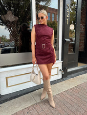 Woman wearing burgundy suede high neck mini dress with belted detail and functional pockets.