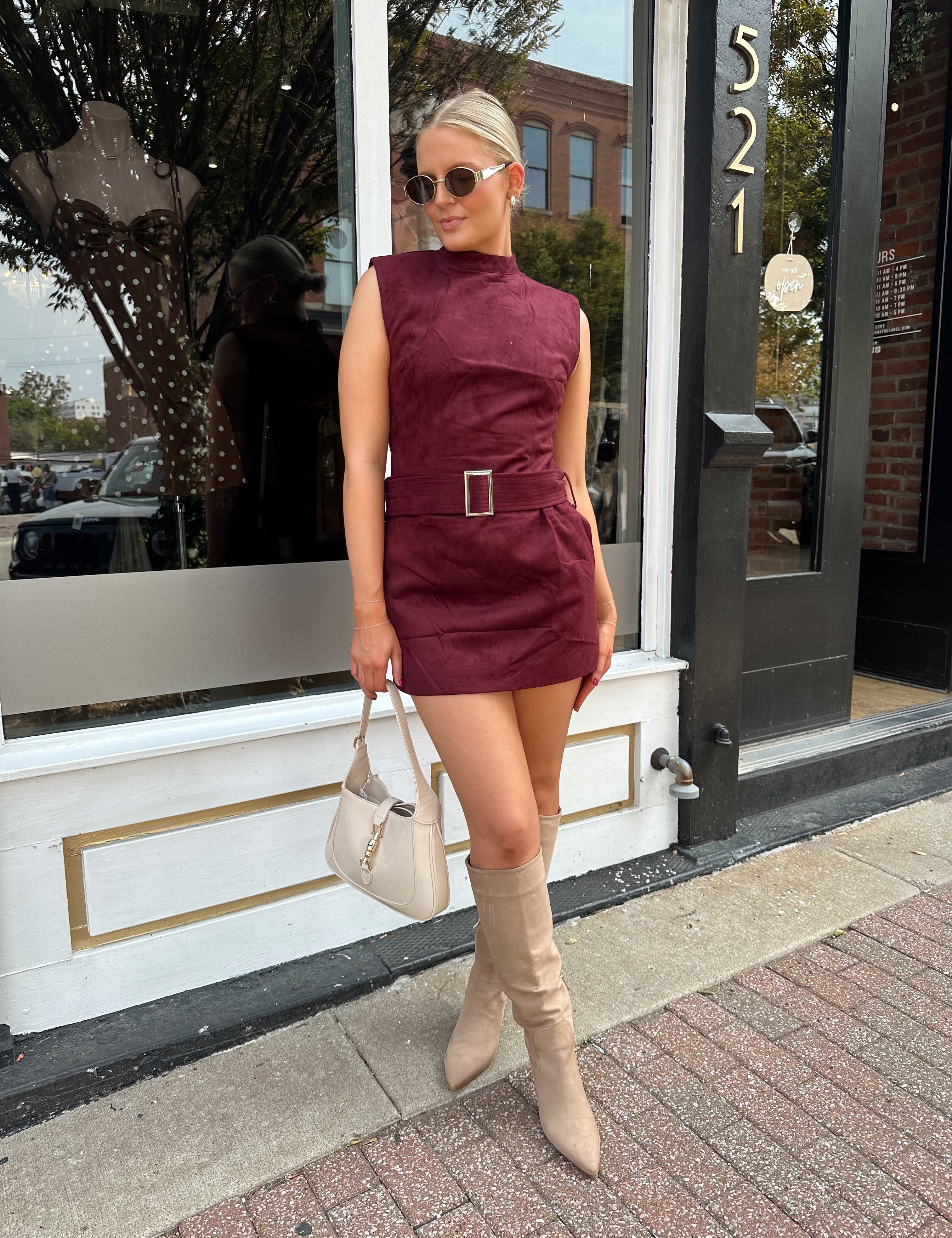 Woman wearing burgundy suede high neck mini dress with belted detail and functional pockets.