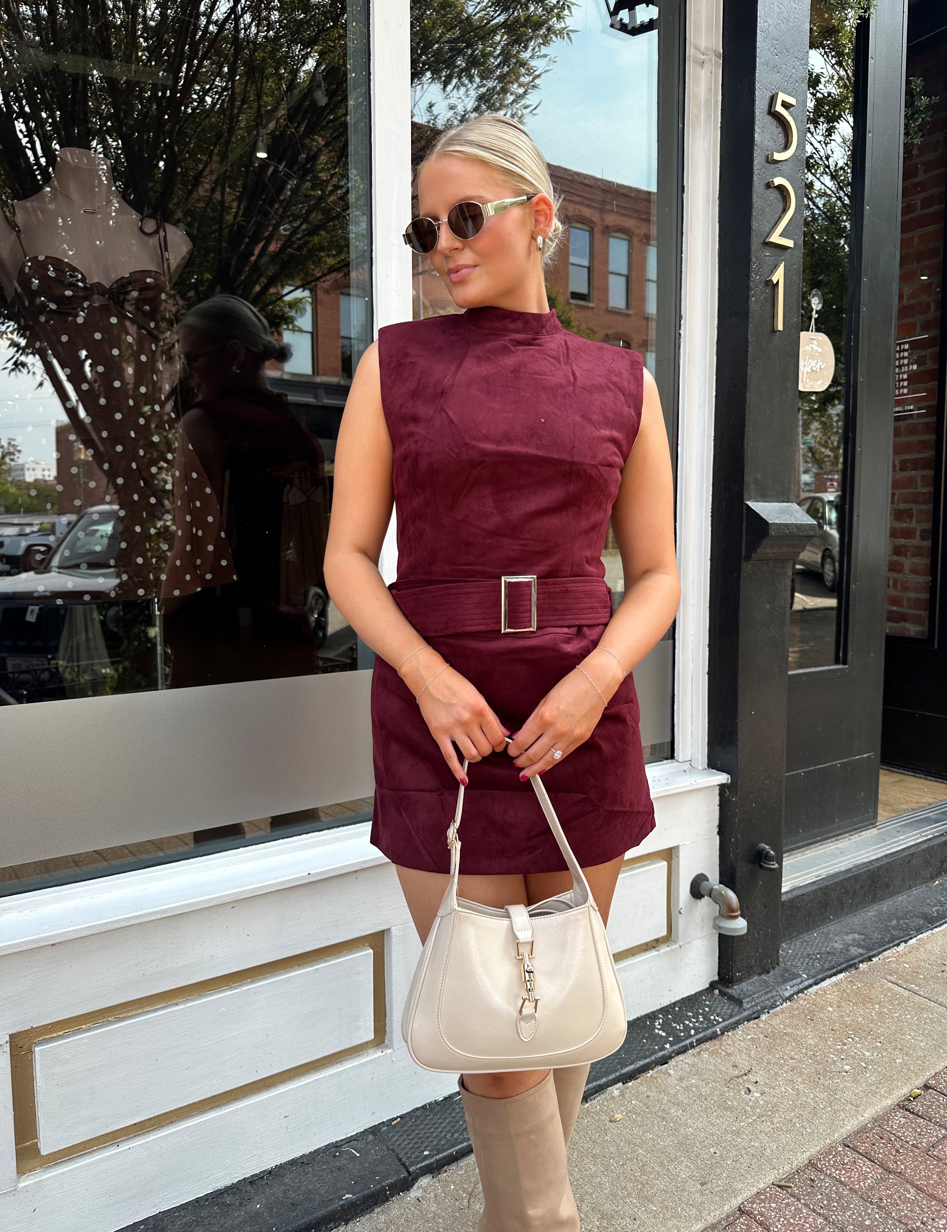 Woman wearing burgundy suede high neck mini dress with belted detail and functional pockets.