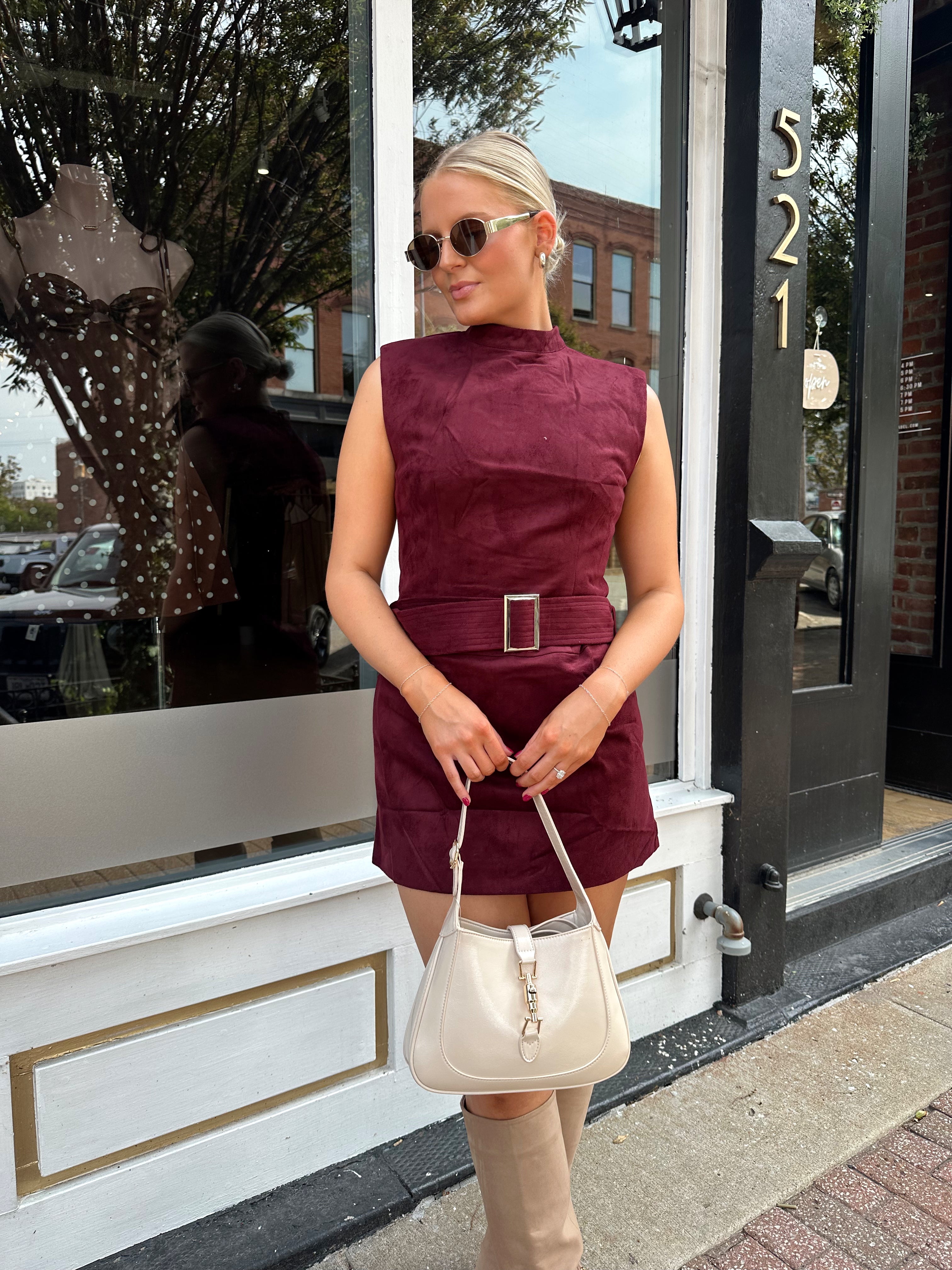 Woman wearing burgundy suede high neck mini dress with belted detail and functional pockets.