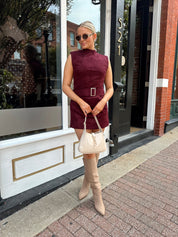 Woman wearing burgundy suede high neck mini dress with belted detail and functional pockets.