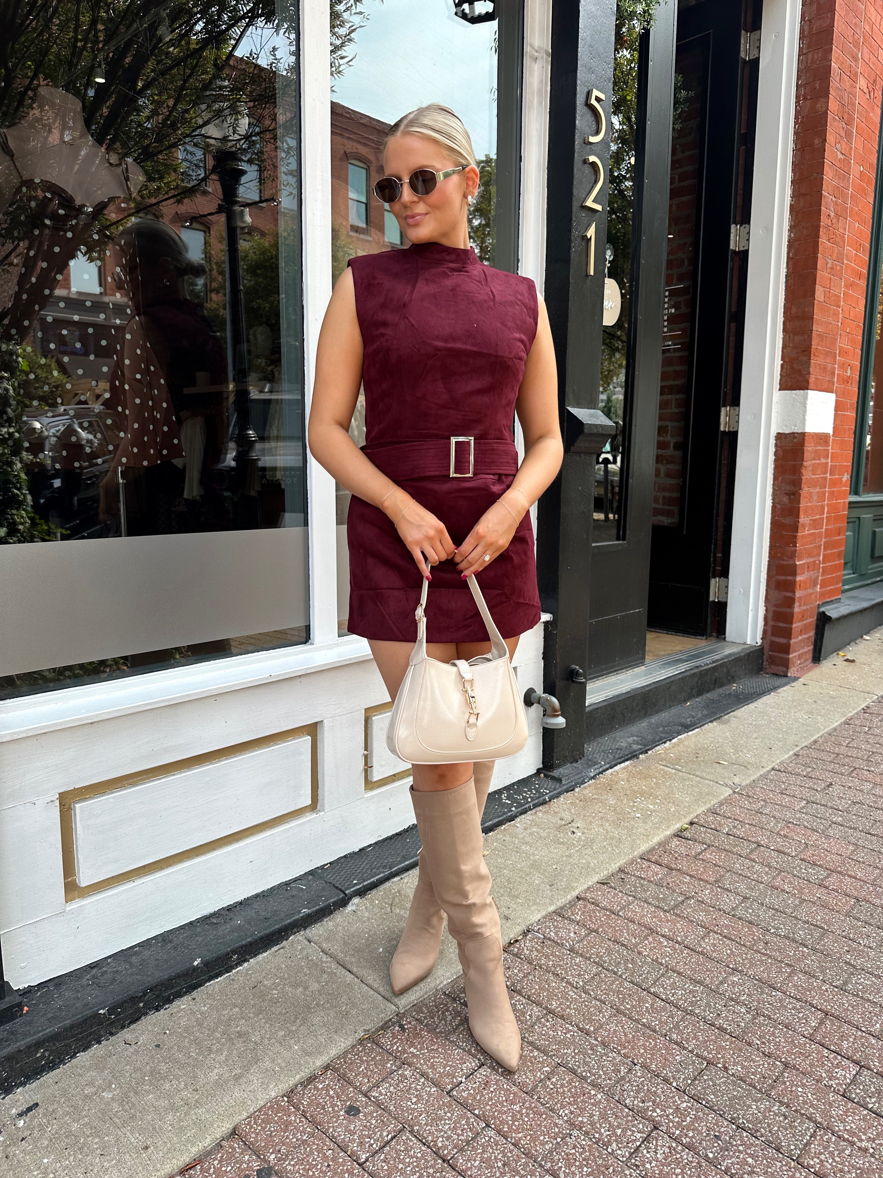 Woman wearing burgundy suede high neck mini dress with belted detail and functional pockets.