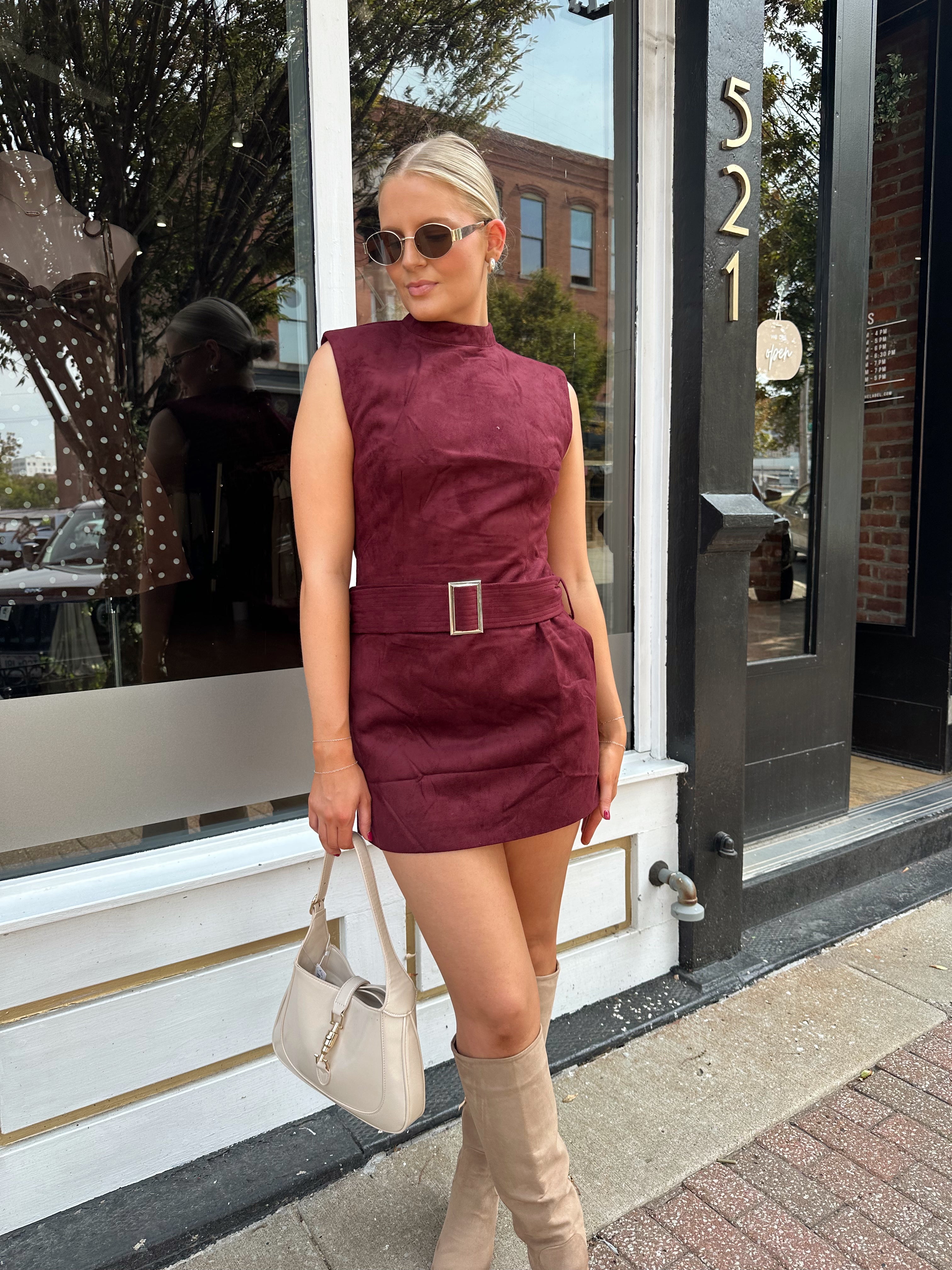 Woman wearing burgundy suede high neck mini dress with belted detail and functional pockets.