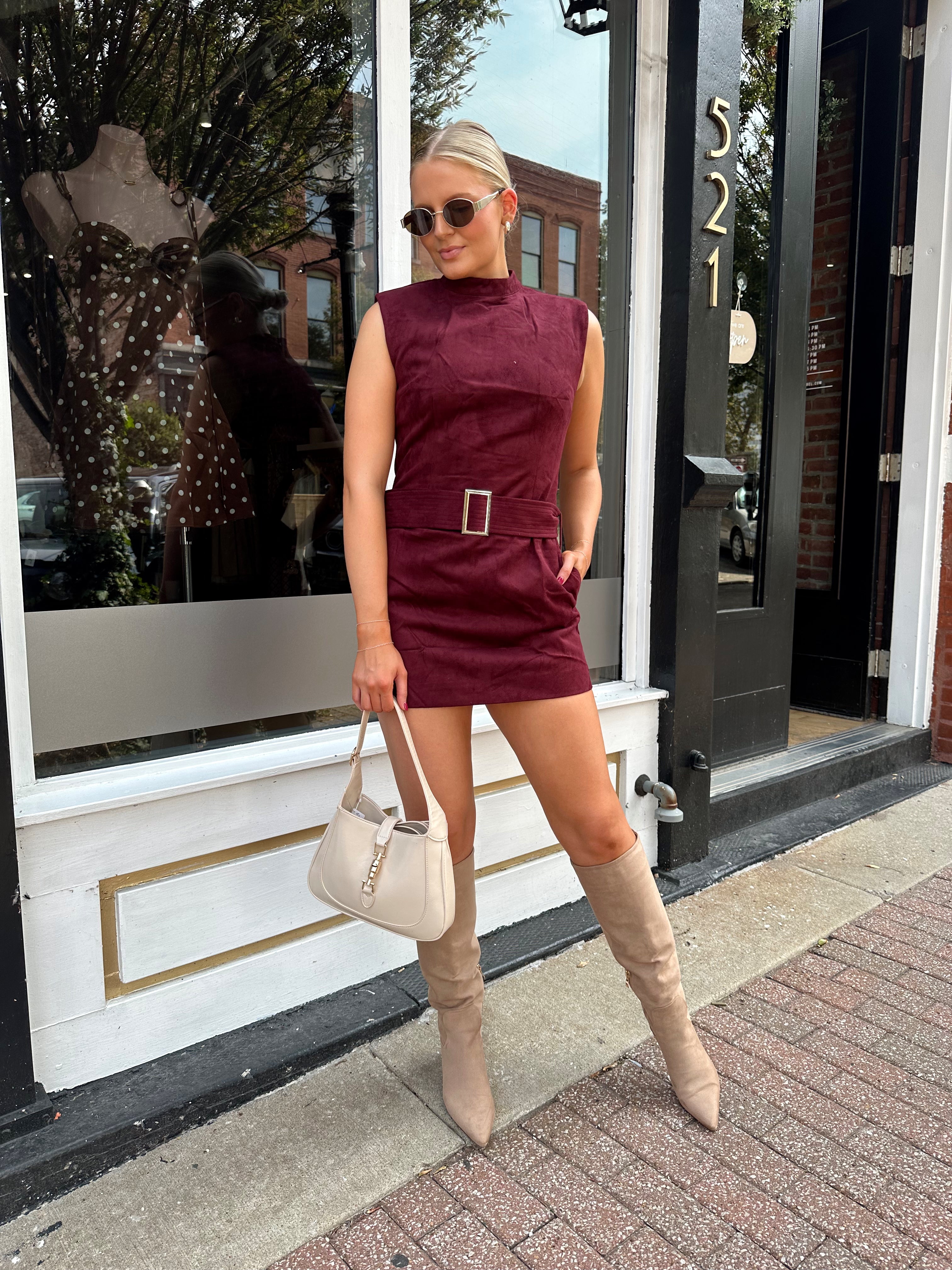 Woman wearing burgundy suede high neck mini dress with belted detail and functional pockets.