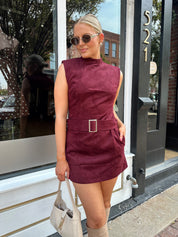Woman wearing burgundy suede high neck mini dress with belted detail and functional pockets.