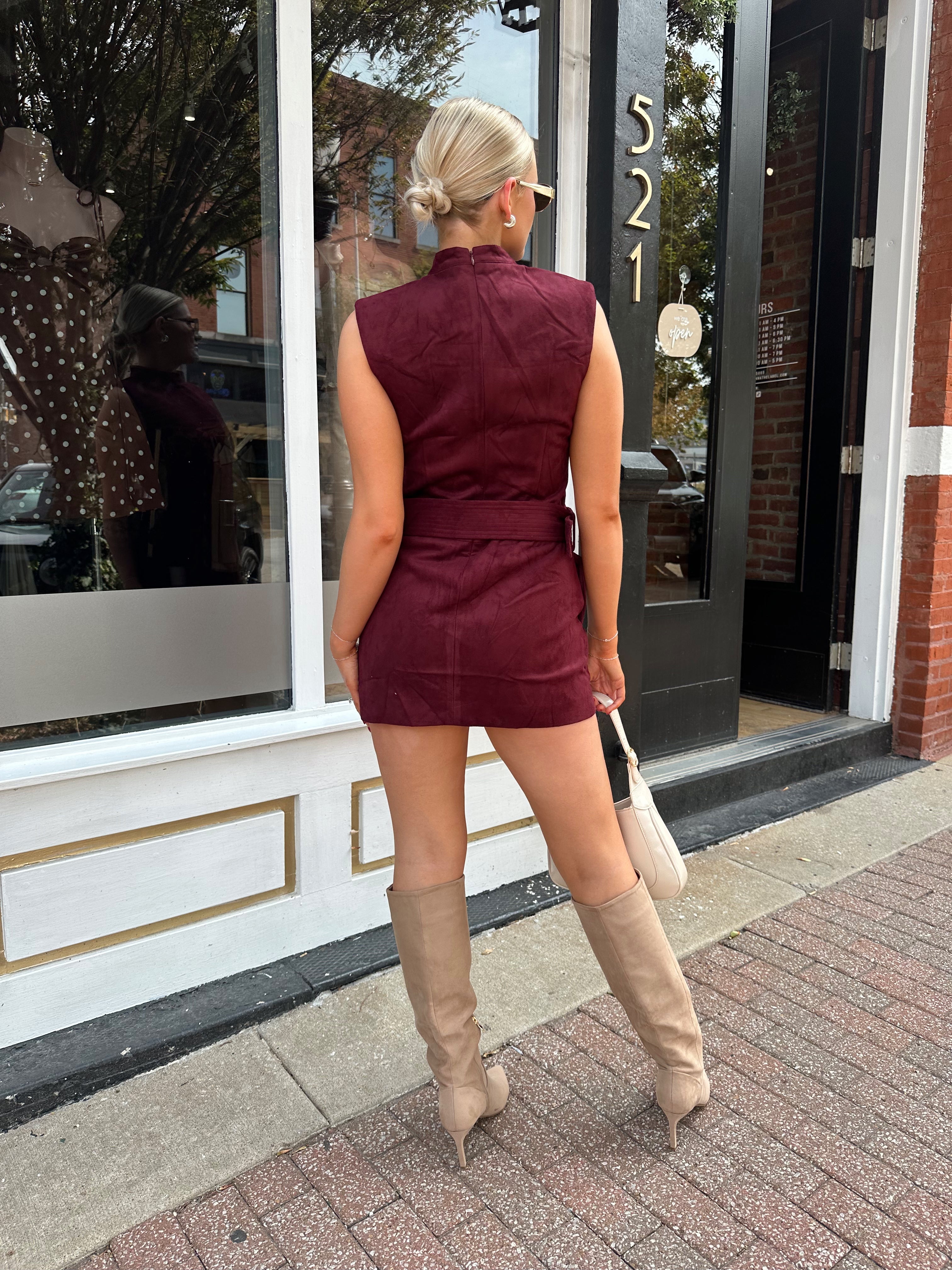 Woman wearing burgundy suede high neck mini dress with belted detail and functional pockets.